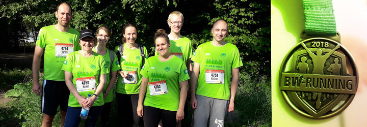 Eine Gruppe von sechs Läufern in grünen Shirts posiert lächelnd vor einem Wald, neben einem Bild einer goldenen Medaille mit der Aufschrift "2018 BW Running".